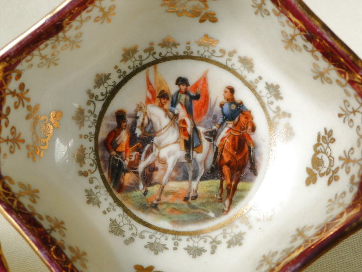 アンティーク雑貨＞アンティーク・陶器＞デミタスカップ＆ソーサー＞白馬にまたがったナポレオンらしき人物の描かれたカップ＆ソーサーです。カップはユニークな八角形。エンジのトリムにゴールドの装飾が華やかなデミタスカップです。
